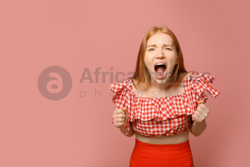 Portrait of angry screaming woman on pink background, space for text