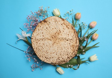 Tasty matzos and fresh flowers on light blue background, flat lay. Passover (Pesach) celebration