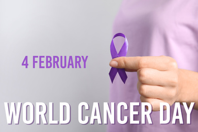 Woman holding purple ribbon against grey background, closeup. World Cancer Day