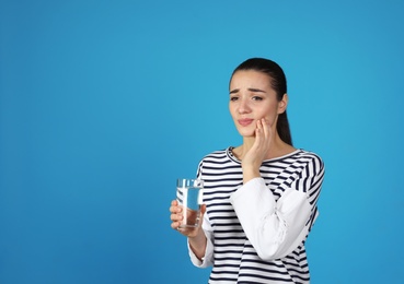 Emotional young woman with sensitive teeth and glass of water on color background. Space for text