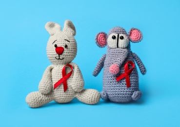 Cute knitted toys with red ribbons on blue background. AIDS disease awareness