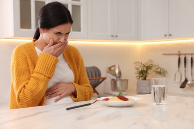 Young woman feeling nausea while seeing food at table in kitchen. Toxicosis during pregnancy