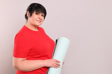 Happy overweight mature woman with yoga mat on grey background, space for text