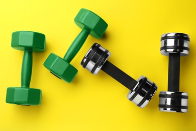 Many different stylish dumbbells on yellow background, flat lay