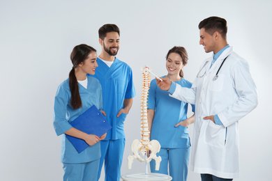 Professional orthopedist with human spine model teaching medical students against light background