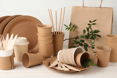 Photo of Eco disposable tableware and green twigs on white wooden table