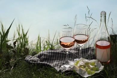 Delicious rose wine, cheese and grapes on picnic blanket near lake, space for text