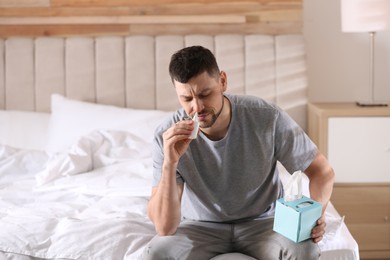 Ill man with nasal spray and box of tissues on bed at home