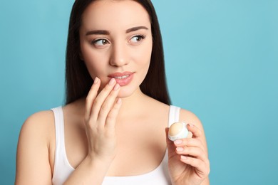 Young woman with lip balm on turquoise background