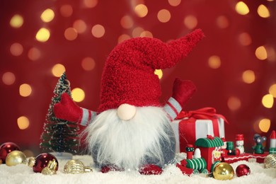 Cute Christmas gnome, gift box and festive decor on snow against blurred lights