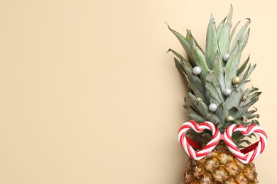Top view of pineapple with funny glasses and festive decor on beige background, space for text. Creative concept