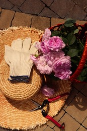 Photo of Basket of beautiful tea roses, straw hat and gardening tools outdoors, flat lay