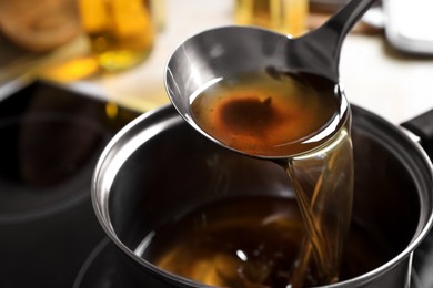 Photo of Pouring used cooking oil with ladle into saucepan on stove, closeup