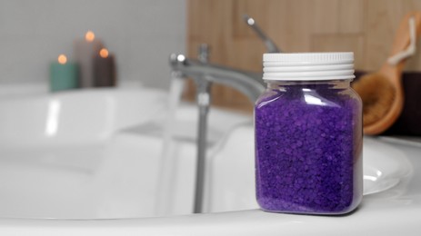 Jar with purple sea salt on bath. Space for text