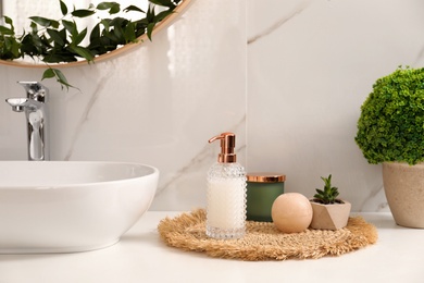 Soap dispenser, plants and candle near vessel sink in bathroom