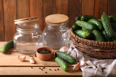 Fresh cucumbers and other ingredients near empty jars prepared for canning on wooden table