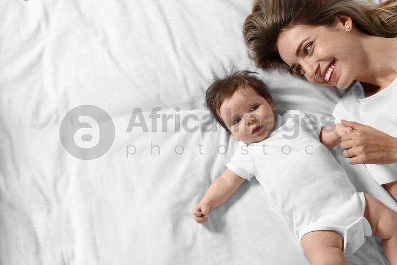Photo of Mother and her little baby lying on bed, top view. Space for text