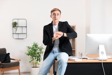 Photo of Emotional man checking time while sitting on table in office. Being late