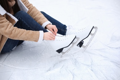 Woman lacing figure skate while sitting on ice, closeup
