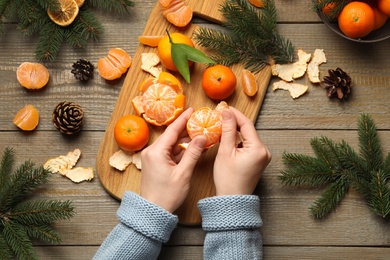 Woman peeling fresh tangerine at wooden table, top view. Christmas atmosphere