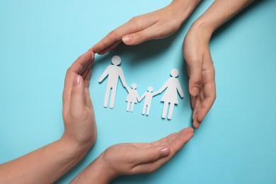 Couple protecting paper family figures on light blue background, top view. Insurance concept