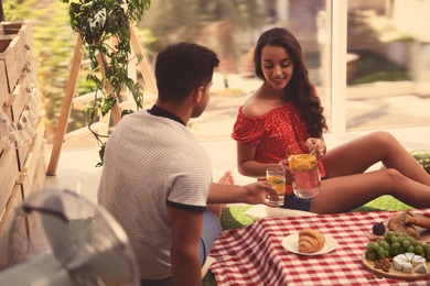 Happy couple with refreshing drink imitating picnic at home