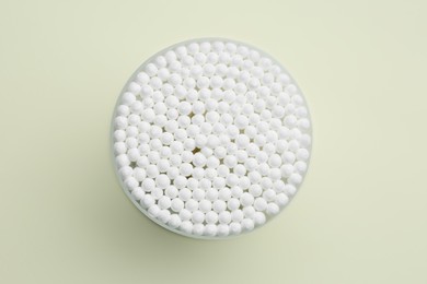 Many cotton buds in container on beige background, top view