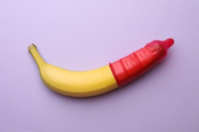 Banana with condom on lilac background, top view. Safe sex concept