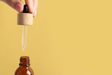 Photo of Woman dripping serum from pipette into bottle on pale orange background, closeup. Space for text