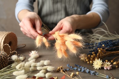 Photo of Florist making bouquet of dried flowers at wooden table, closeup