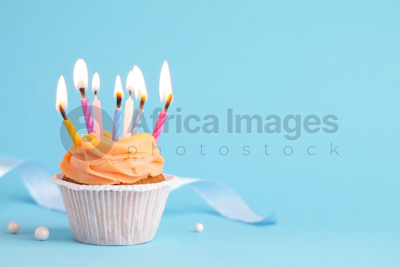 Tasty birthday cupcake with many candles on light blue background. Space for text