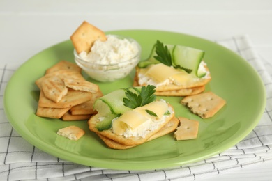 Delicious crackers with cream cheese, cucumber and parsley on white table, closeup