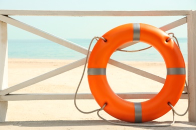 Orange life buoy near wooden railing on beach.  Emergency rescue equipment