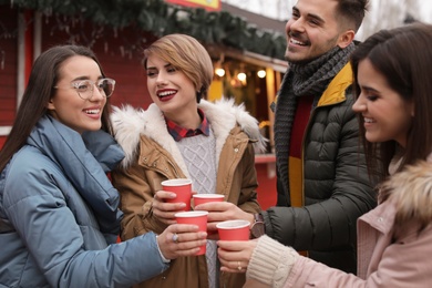 Happy friends with cups of mulled wine at winter fair