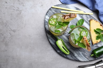 Photo of Glasses of spicy pineapple cocktail with jalapeno and mint on grey table, flat lay. Space for text