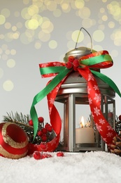 Decorative lantern and Christmas decor on snow against festive lights