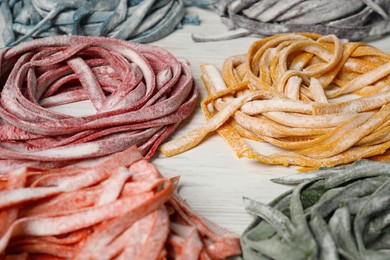 Photo of Rolled pasta painted with different food colorings on white wooden table, closeup