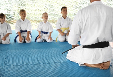Children and coach sitting on tatami outdoors. Karate practice