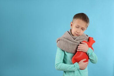 Ill boy with hot water bottle suffering from cold on light blue background, space for text