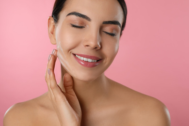 Photo of Young woman applying cosmetic product on pink background, closeup. Washing routine