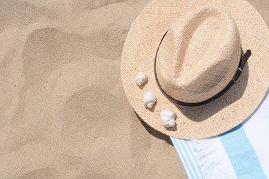Straw hat with seashells and beach towel on sand, top view. Space for text