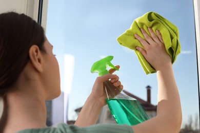 Young woman cleaning window glass with rag and detergent at home, closeup
