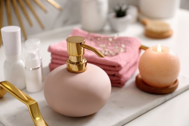 Tray with soap dispenser, burning candle and towels on countertop in bathroom, closeup