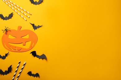 Flat lay composition with spooky paper pumpkin, bats and straws on yellow background, space for text. Halloween celebration