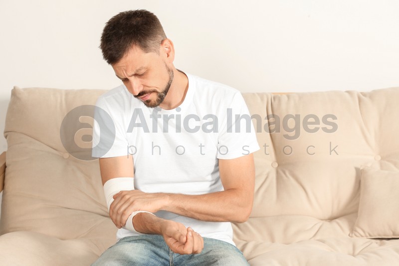 Photo of Man with arm wrapped in medical bandage on sofa indoors