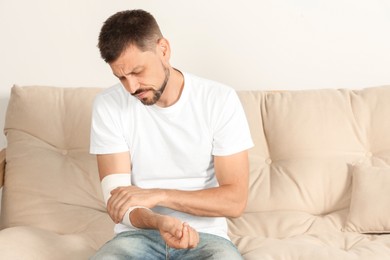 Man with arm wrapped in medical bandage on sofa indoors
