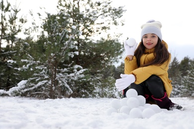 Cute little girl rolling snowballs in winter forest