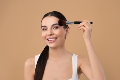 Photo of Beautiful woman applying makeup on light brown background