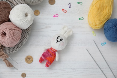 Crocheted bunny and knitting supplies on white wooden table, flat lay. Engaging in hobby