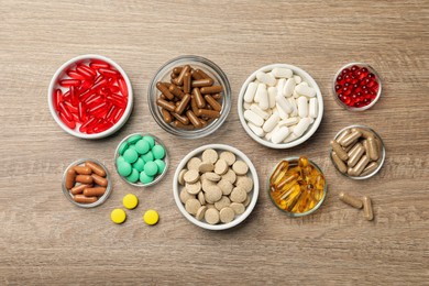 Different dietary supplements in bowls on wooden table, flat lay